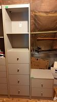 Tall white cabinet with four drawers and one adjustable shelf, next to smaller two drawer cabinet, both white with round knobs.