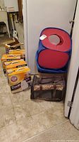 Photo showing the collapsible blue and red cat toy tunnel, brown soft-sided cat carrier with leopard print, white plastic litter box, and four boxes of Arm & Hammer cat litter on floor