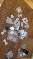 Photo showing assorted coins scattered on a wooden surface including coins in plastic holders and possibly coin tubes.