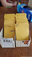 Two white boxes filled with numerous yellow envelopes labeled with various British and Canadian coin types and years, placed on a wooden table.