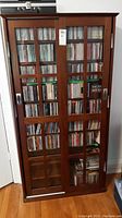 Front view of wood display case with sliding glass doors and visible interior shelves containing CD cases (contents not included).