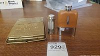 Brass lantern folded flat alongside a small metal flask covered in brown leather and a silver-tone cylindrical match holder.