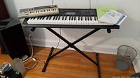 Two keyboard models set on an adjustable stand, a larger CTK-3200 and a smaller PT-50, with power cord visible and a speaker in the background.