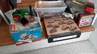 Summary of lot from wide angle showing all items on floor: green steam tractor model, Wilesco box, plastic model tanks, silver model cars, red toy truck, 1940 BMW 328 tin container