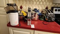 Full view of the lot on a red counter, showing all items: pressure cooker, apple spiraler, toaster, blender, popcorn machine