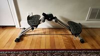 Full side view of the sideways stepper machine on a wooden floor showing metal frame, wide foot pedals, and overall design.