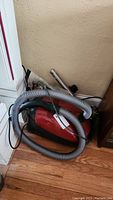 Red Miele canister vacuum body with attached grey hose and telescoping wand against wall
