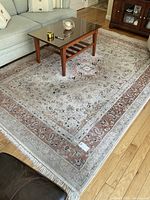 Large cream-toned area rug with intricate central medallion pattern and fringed edges under a glass coffee table