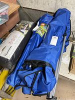 Multiple camping items in storage showing wrapped blue chairs and packaged 12x12 screenhouse on floor with dustpan nearby.