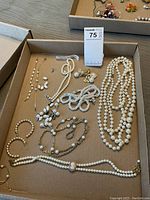 Top-down view of assorted costume jewelry including pearl necklaces, bracelets, earrings, and a brooch in a box.