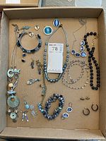 Box with assorted costume jewelry including necklaces, bracelets, and earrings in various blue, silver, and gold tones.