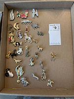 Box of assorted costume jewelry pins arranged in rows inside a cardboard box.