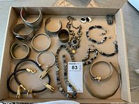 Top-down photo of assorted costume jewelry in a cardboard box showing multiple bracelets, necklaces, earrings, and a small coin purse.