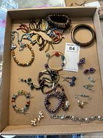Top view of assorted costume jewelry including necklaces, bracelets, earrings, and pins inside a cardboard tray.