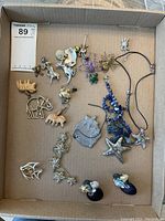 Top view of assorted costume jewelry including aquatic and animal-themed pieces like necklaces, bracelets, pins, and earrings arranged in a cardboard box.