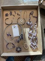 Top-down photo showing assorted costume jewelry including necklaces, bracelets, earrings, and a brooch pin on a cardboard surface.