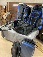 Assorted luggage and bags placed on a bed and floor including duffel bags and the hard case suitcase.