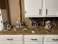 Wide shot of nativity village displayed on grass mats, showing multiple buildings and figures arranged in a scene.
