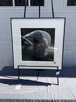 Framed black and white photo art depicting an abstract shape on display stand outdoors.