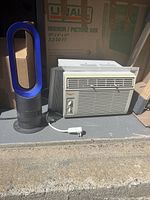 Dyson bladeless tower fan and Ocean Breeze window air conditioner side by side on concrete floor.