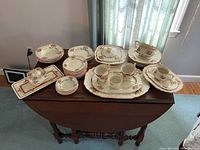 Full set of white and beige china pieces featuring floral brown borders, displayed on a table.
