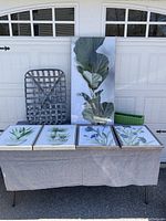 Full view showing all five botanical wall art pieces displayed on a table with two woven baskets behind them.