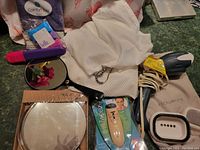 Photo showing assortment of bathroom personal care items including unopened tweezer, hair steamer in beige pouch, pink and purple hair styling tool, round black handled mirror, and white cloth.