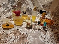 Wide shot of 11 assorted perfume bottles on lace fabric backdrop, showing variety in bottle shapes, sizes and colors.