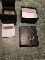 Photo of the ladies ring and fine chain necklace placed on top of a black jewelry box with an open lid, displaying both items clearly with the box background.