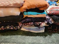 Stack of folded clothing showing various tops, sweaters, and scarves in different colors and patterns