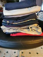 Stack of folded ladies bottoms on a black cushioned chair showing variety of colors and materials