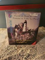Photo of the boxed fountain showing branding and product name in three languages: English, Spanish, and French. The box image depicts the lighthouse fountain with rocks and foliage.