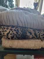Stack of three throw blankets including a grey blanket on top, leopard print in middle, and beige underneath