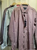 Three men's dress shirts hanging on wooden hangers showing different patterns and colors.