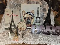 Photo showing the Paris decor items arranged on lace fabric, including two Eiffel Tower replicas, a clock, a Paris sign, and a bulldog painting.