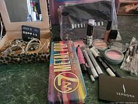 Lot spread featuring brand new cosmetics including palettes, lip gloss, lipsticks, mascaras along with a leopard print case containing jewelry items.