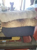 Photo of three throw blankets stacked: grey plush on top, brown plush in the middle, navy knit on bottom with some pulls visible.