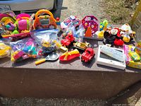 Various colorful children's toys laid out including trucks, educational electronics, figurines, and play sets
