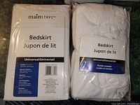 Two identical white universal bedskirts by Mainstays; one in original packaging, the other tried and repackaged