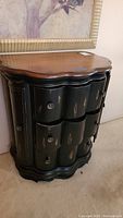 Full view of black woodgrain Bombay styled side table with curved front and three drawers.