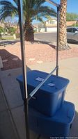 Full view of metal adjustable clothes rack and two stacked blue storage totes outdoors.