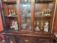 Wooden display cabinet with two bottom shelves containing various crystal and cut glass items including decanters, stemware, candlestick holders, bowls, and trays.