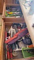 Photo of two kitchen drawers filled with assorted utensils and a variety of knives with colored protective sheaths, ladle, and scissors.