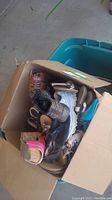 Open cardboard box filled with various ladies shoes including athletic sneakers, sandals, and heels in different colors and styles.