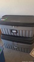 Two stacked gray Rubbermaid storage totes with black lids, showing size and overall condition.