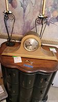 Front view of the wooden Ingraham mantle clock on a wooden table with two winding keys placed in front.