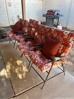 Four folding patio chairs with floral patterned cushions and two red throw pillows, arranged outdoors on patio.