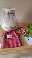 Full view of ceramic pot, woven dolls, and striped sack arranged on a wooden surface.