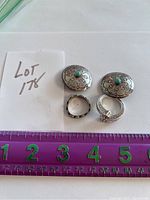 Four silver jewelry pieces displayed with a ruler for scale: two rings and a pair of round, domed earrings with turquoise stones and engraved designs