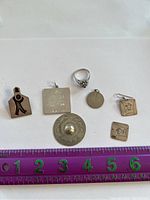 Silver pieces on a white surface with ruler for scale, showing a ring, pendants, brooch, and earrings